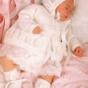 May include: A white knitted baby outfit set with a cardigan, hat, and booties. The set features a delicate leaf pattern and is made with a soft yarn.