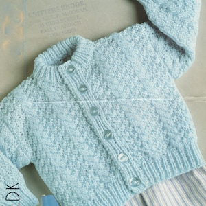 May include: A light blue knitted cardigan with a button closure and a cable knit pattern. The cardigan is laid flat on a striped surface.