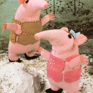 Puede incluir: Dos animales de peluche de punto rosa con narices largas y ojos marrones. El animal de la izquierda lleva un chaleco marrón con botones dorados. El animal de la derecha lleva un chaleco rosa con botones blancos y un lazo azul. Los animales están de pie sobre una superficie blanca con pequeñas piedras grises.