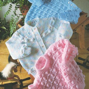 Può includere: Tre maglioni di lana per neonati in diversi colori: azzurro, rosa e un motivo multicolore. I maglioni hanno un design testurizzato e con effetto 'bobbly'.