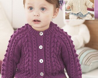 May include: A purple knitted cardigan with a cable knit pattern and button closure. The cardigan is worn by a child and has a floral headband.