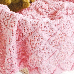 May include: A pink knitted baby blanket with a delicate cable stitch pattern.