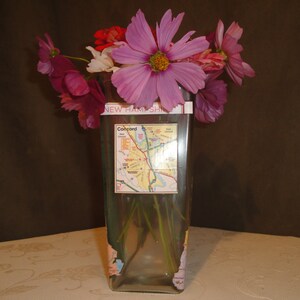 May include: A clear glass vase with a map of Concord, New Hampshire, on the front. The vase is filled with pink and purple flowers.