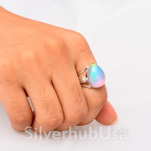 Könnte beinhalten: Ein silberner Ring mit einem tropfenförmigen, schillernden Edelstein. Der Edelstein ist hellblau mit einem Hauch von Rosa und Lila.