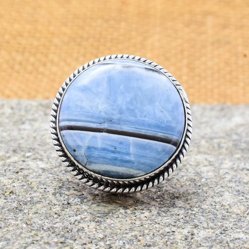 May include: A silver ring with a blue and black agate stone set in a rope-like design.