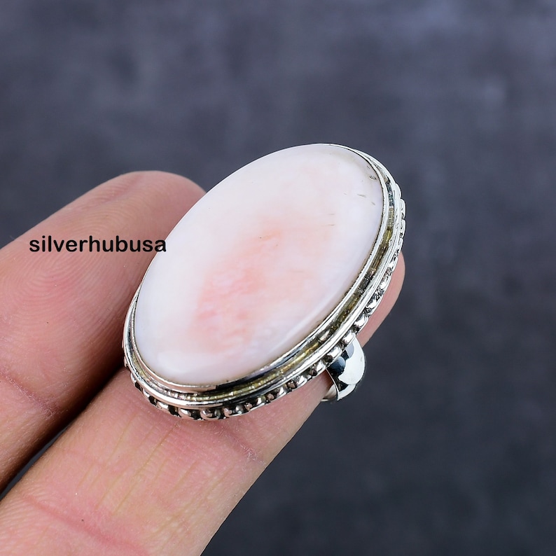 May include: A silver ring with a large oval pink opal gemstone. The ring has a beaded edge around the stone.