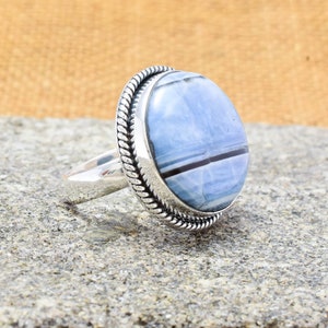 May include: A silver ring with a blue and black banded agate stone set in a rope-like bezel.