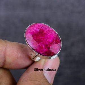 May include: A silver ring with a large, oval-shaped, pink ruby gemstone. The ring is set in a simple, silver band.