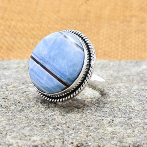 May include: A silver ring with a blue and white opal stone set in a rope-like band.