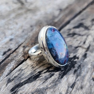Peut inclure: Une bague en argent avec une pierre ovale bleue et rouge sertie dans un sertissage à bélière.