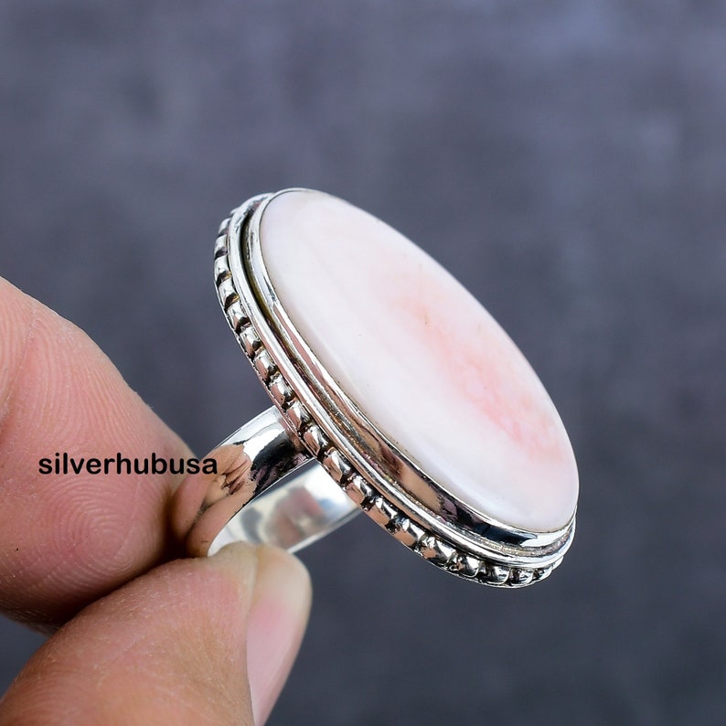 May include: A silver ring with a large oval pink and white shell cameo. The ring has a beaded edge.