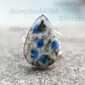May include: A silver ring featuring a teardrop-shaped blue and white stone. The stone has a speckled pattern with blue flecks.