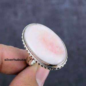 May include: A silver ring with a large oval pink and white gemstone set in a beaded bezel.