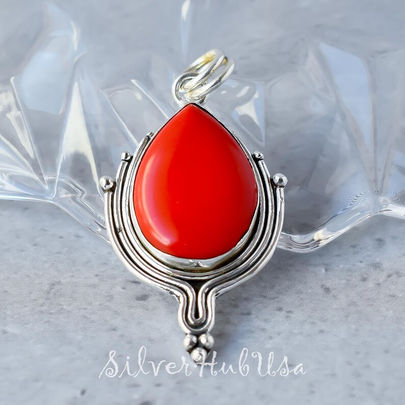 Puede incluir: Un colgante de piedra preciosa de coral rojo con un engaste de plata. El colgante tiene forma de l&aacute;grima y un dise&ntilde;o detallado.