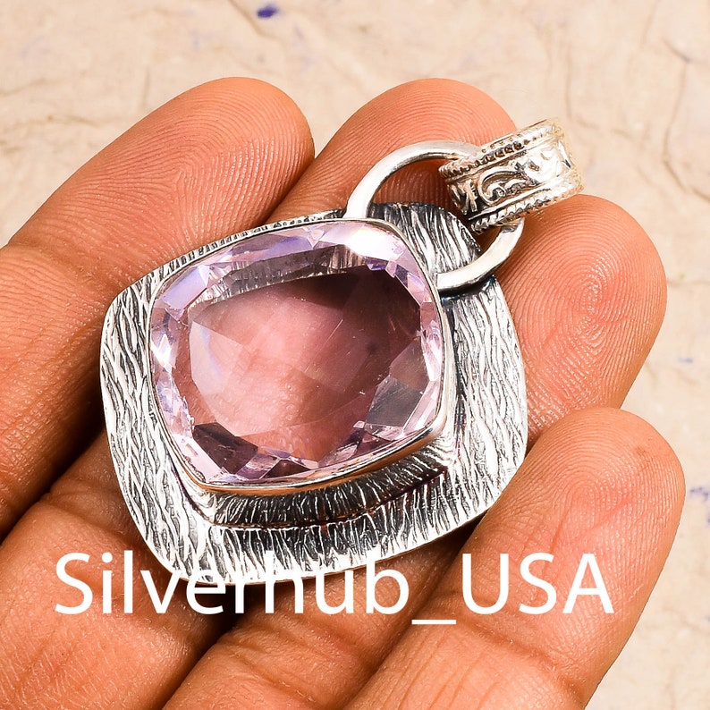 Peut inclure: Un pendentif en argent avec une pierre pr&eacute;cieuse violette clair sertie dans un cadre en argent textur&eacute;. Le pendentif a un b&eacute;li&egrave;re avec un motif orn&eacute;.