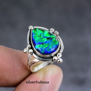 Op de afbeelding: Een zilveren ring met een peervormige, iriserende edelsteen met levendige groene en blauwe tinten. De ring heeft een gedetailleerde zetting met kleine, decoratieve zilveren accenten. De tekst "silverhubusa" is zichtbaar onderaan.