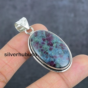 May include: Oval shaped pendant with a green and purple gemstone set in sterling silver. The gemstone has a mottled pattern of green, purple, and white.