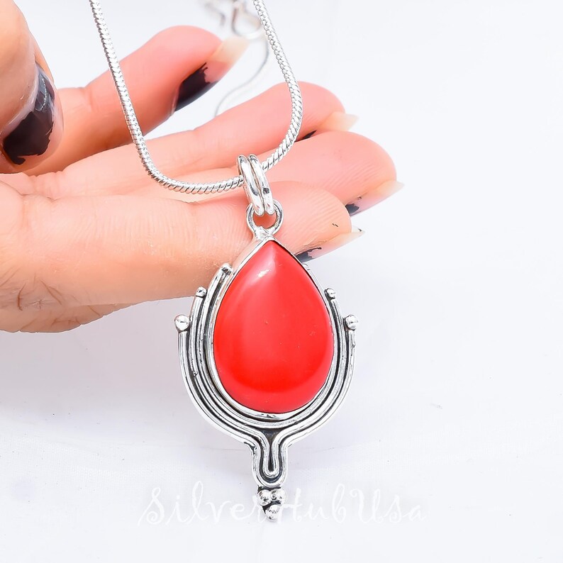 Puede incluir: Un collar de cadena de plata con un colgante de piedra roja. El colgante tiene forma de l&aacute;grima y un dise&ntilde;o de filigrana de plata.