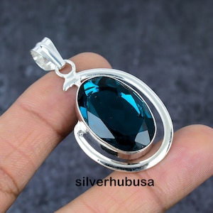 Puede incluir: Un colgante de plata con una gran piedra preciosa ovalada de color azul turquesa engastada en un marco de plata. El colgante tiene un aro para sujetarlo a una cadena.