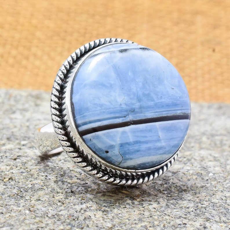 May include: A silver ring with a blue and black agate stone set in a rope-like design.