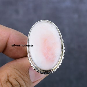 May include: A silver ring with a large oval pink opal gemstone. The ring has a beaded edge around the stone.