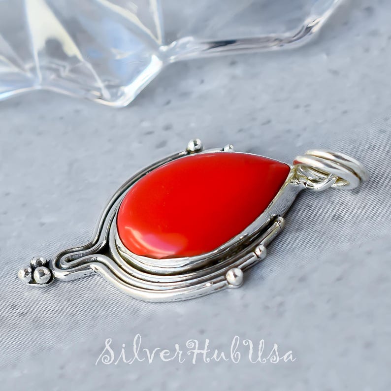 Puede incluir: Un colgante de plata con una piedra preciosa roja brillante en forma de l&aacute;grima. El colgante tiene un dise&ntilde;o delicado y ornamentado con m&uacute;ltiples capas de plata.