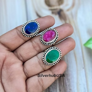 May include: Three silver rings with oval-shaped gemstones. The rings have a beaded design around the edges. The gemstones are blue, red, and green.