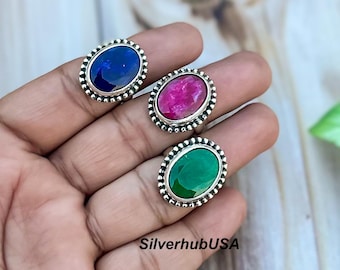 May include: Three silver rings with oval-shaped gemstones. The rings have a beaded design around the edges. The gemstones are blue, red, and green.