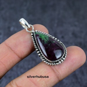 Può includere: Un ciondolo a forma di lacrima con una pietra preziosa verde e viola incastonata in una cornice d'argento con un motivo a corda intrecciata.