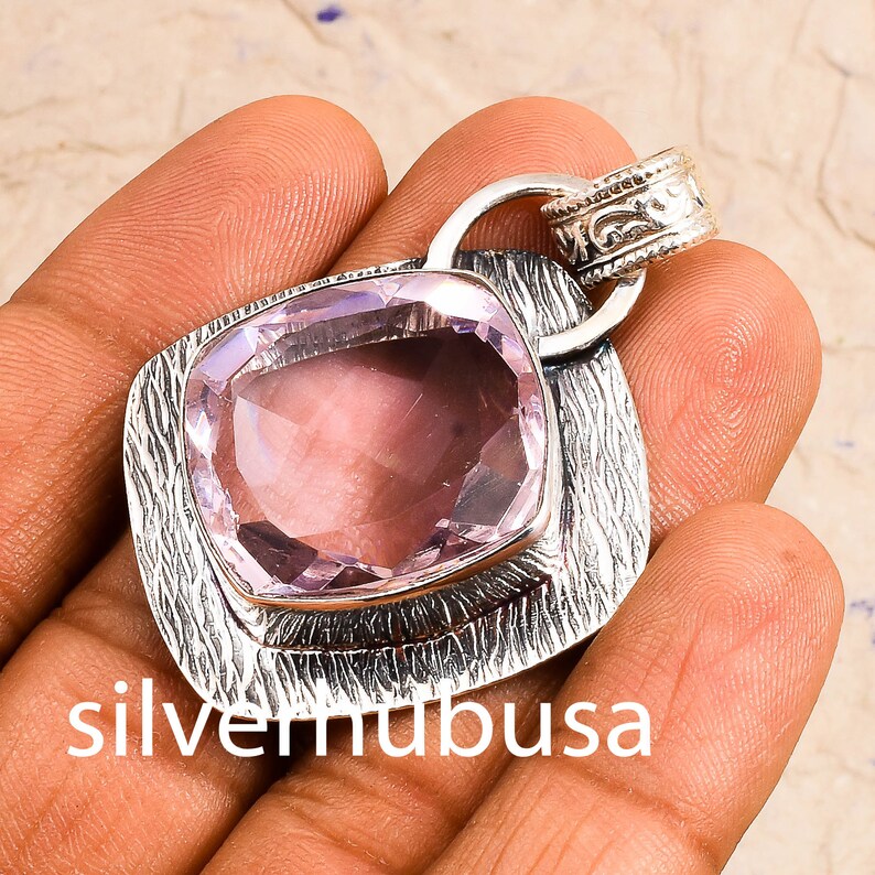 Peut inclure: Un pendentif en argent avec une pierre pr&eacute;cieuse violette clair. Le pendentif a un design textur&eacute; et une b&eacute;li&egrave;re avec un design orn&eacute;.