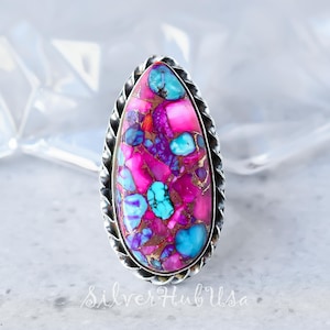 May include: A silver ring with a large, teardrop-shaped stone. The stone is a mix of pink, purple, turquoise, and gold colors. The ring has a twisted band.