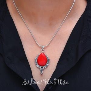 Puede incluir: Un collar de cadena de plata con un colgante de piedra roja. El colgante tiene forma de l&aacute;grima y presenta un dise&ntilde;o de filigrana de plata.