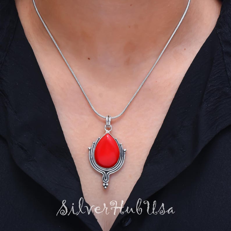 Puede incluir: Un collar de cadena de plata con un colgante de piedra roja. El colgante tiene forma de l&aacute;grima y presenta un dise&ntilde;o de filigrana de plata.