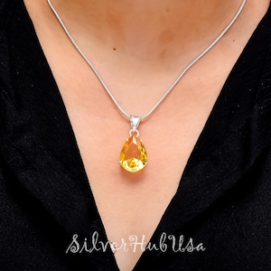 Könnte beinhalten: Eine silberne Kettenkette mit einem tropfenförmigen Anhänger mit einem gelben Edelstein.