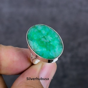 Peut inclure: Une bague en argent avec une grande pierre précieuse ovale verte. La bague est sertie d'une simple bande.