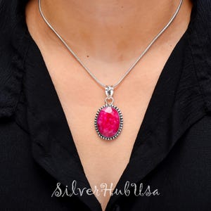 Pode incluir: Um colar de corrente de prata com um pingente oval de pedra rosa. O pingente tem uma borda de prata com pequenas contas.