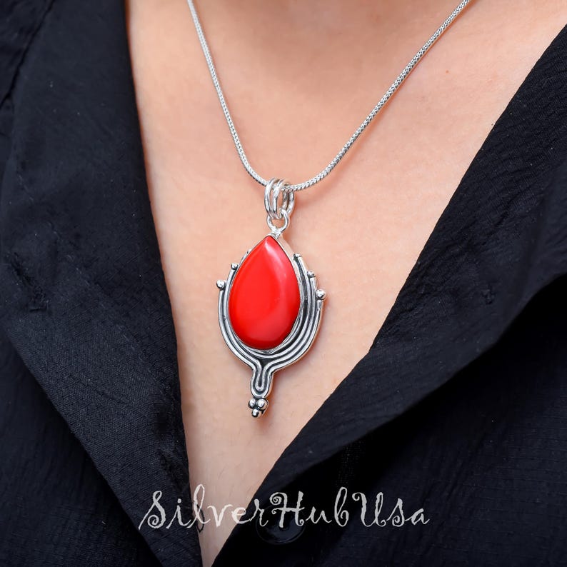 Puede incluir: Un collar de plata con un colgante rojo en forma de l&aacute;grima. El colgante est&aacute; engastado en un marco de plata con detalles intrincados.