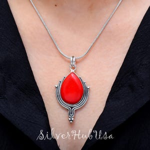 Puede incluir: Un collar de plata con un colgante de piedra roja. El colgante tiene forma de l&aacute;grima y presenta intrincados detalles de plata.