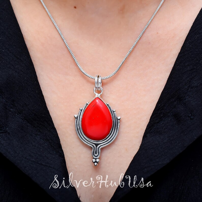 Puede incluir: Un collar de plata con un colgante de piedra roja. El colgante tiene forma de l&aacute;grima y presenta intrincados detalles de plata.