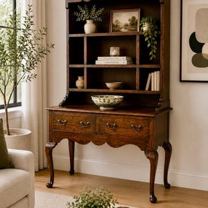 May include: A tall, dark brown wooden dresser featuring an open shelving unit with multiple compartments above a base with two drawers. The piece has curved legs and scalloped apron detailing, displaying various decorative items on its shelves.