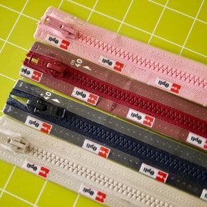 Könnte beinhalten: Fünf verschiedene Reißverschlussbänder mit einem 40 cm Etikett auf jedem. Die Bänder sind rosa, rot, grau, marineblau und beige.