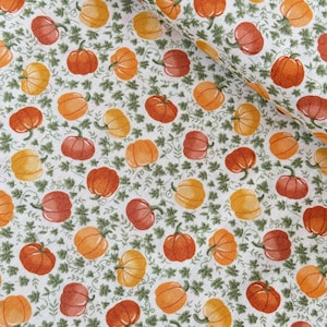 May include: White fabric featuring a repeating pattern of pumpkins in orange, yellow, and red hues. Green vines and leaves are scattered amongst the pumpkins, creating a harvest theme.