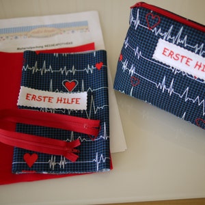 Könnte beinhalten: Ein Erste-Hilfe-Set-Projekt mit blauem Stoff mit weißem EKG-Muster und roten Herzen. Das Set enthält einen roten Reißverschluss, roten Stoff und ein Etikett mit der Aufschrift "ERSTE HILFE".