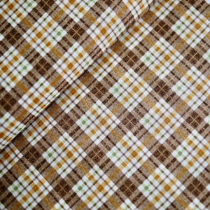 Könnte beinhalten: Nahaufnahme eines Stoffes mit Karomuster. Das Design zeigt ein sich wiederholendes Muster aus braunen, weißen, gelben und grünen Quadraten und Linien. Der Stoff ist gefaltet und zeigt das Muster aus verschiedenen Blickwinkeln.