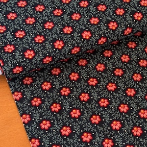 Op de afbeelding: Donker marineblauwe stof met een herhalend bloemmotief. Het ontwerp bevat rode bloemen met gele centra, groene bladeren en kleine witte stippen. De stof is gevouwen, waardoor de herhaling van het patroon zichtbaar is.