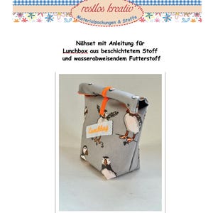 Könnte beinhalten: Eine graue Lunchbox mit einem Papageientaucher-Muster. Sie hat einen orangefarbenen Verschlussriemen und ein Etikett mit der Aufschrift "Lunchbag". Der Text "restlos kreativ Materialpackungen & Stoffe" befindet sich oben.