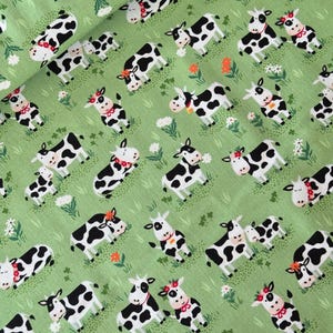 Könnte beinhalten: Grüner Stoff mit einem sich wiederholenden Muster von Cartoon-Kühen in Schwarz und Weiß. Einige Kühe haben florale Akzente und rote Schleifen. Der Hintergrund zeigt kleine Blumen und Gras.