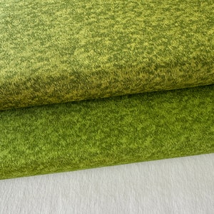 Könnte beinhalten: Nahaufnahme eines grünen Stoffes mit einer strukturierten, gesprenkelten Musterung. Der Stoff ist in der Mitte gefaltet und zeigt darunter eine hellere grüne Farbe.