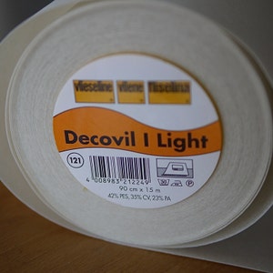 Könnte beinhalten: Eine Rolle weißer Decovil I Light-Vlieseline mit einem Etikett, auf dem "Decovil I Light" steht und der Produktcode "121", der Barcode und die Größe "90 cm x 15 m" angegeben sind. Das Etikett enthält auch die Stoffzusammensetzung: "42% PES, 35% CV, 23% PA".