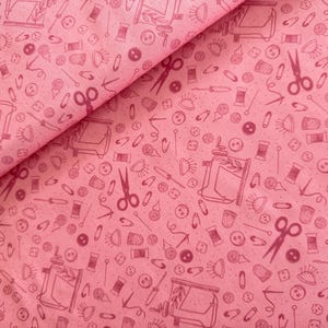 Pode incluir: Tecido rosa com um padrão repetido de ilustrações com tema de costura. O padrão inclui máquinas de costura, botões, agulhas, carretéis de linha, tesouras e alfinetes de segurança.